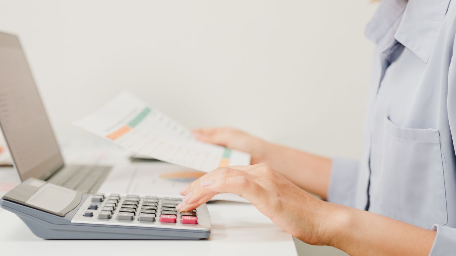 Eine Ärztin sitzt vor dem Laptop und tippt eine Zahl in ihren Taschenrechner