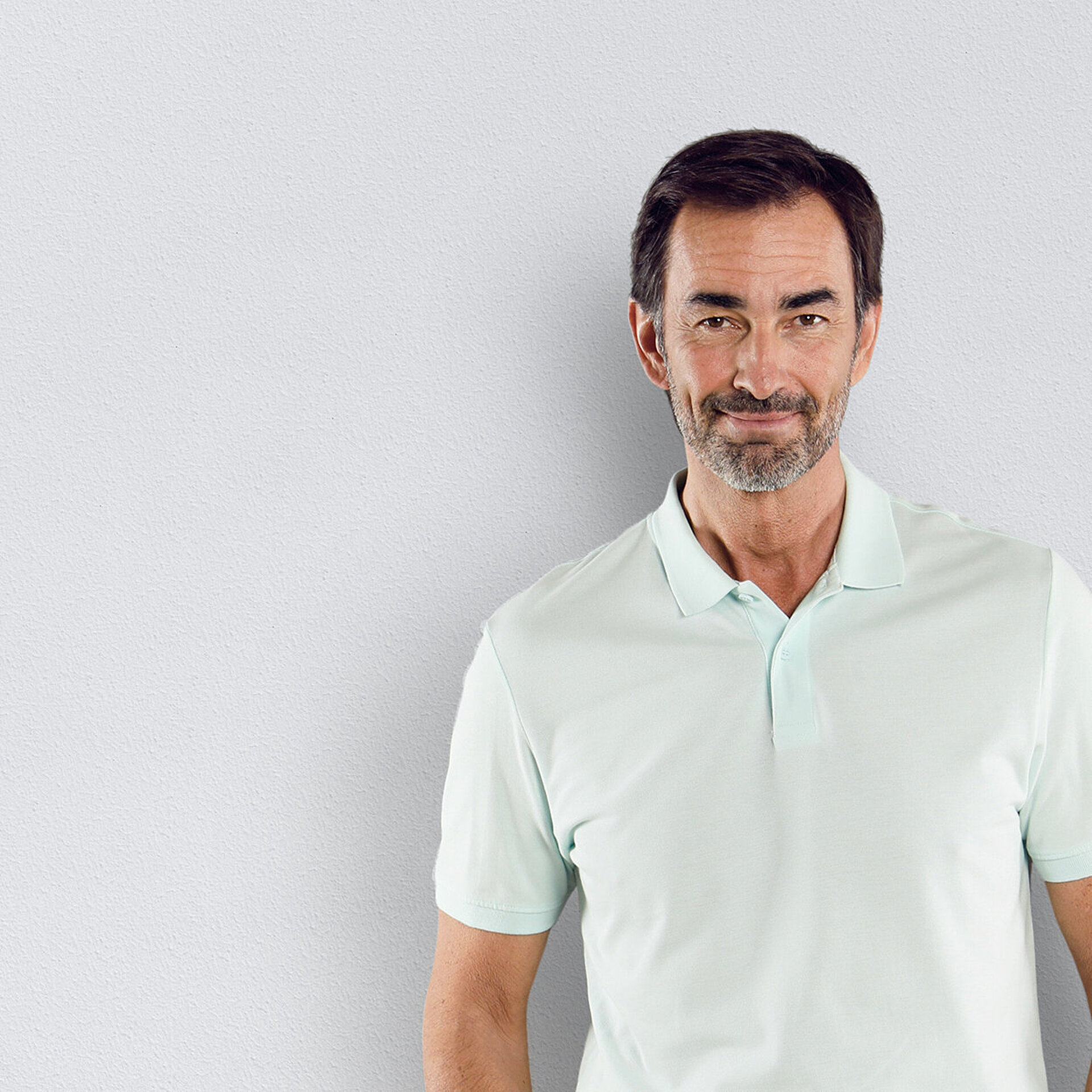 Ein Kardiologe im Poloshirt steht vor einer weißen Wand.