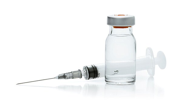 Eine Ampulle mit einer durchsichtigen Flüssigkeit steht vor einer Spritze