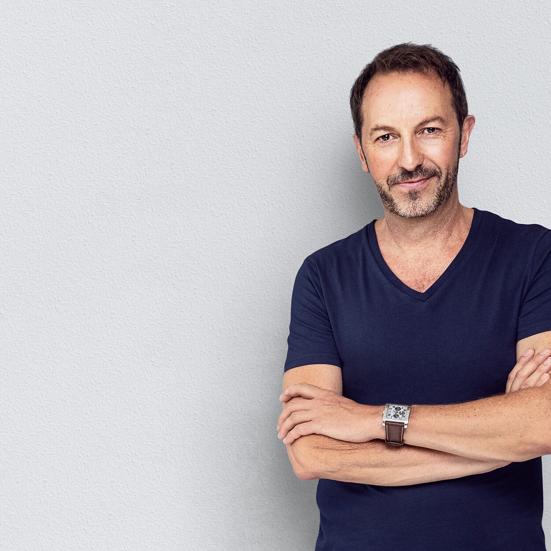 Ein Urologe lehnt sich an einer Wand mit weißer Tapete an.