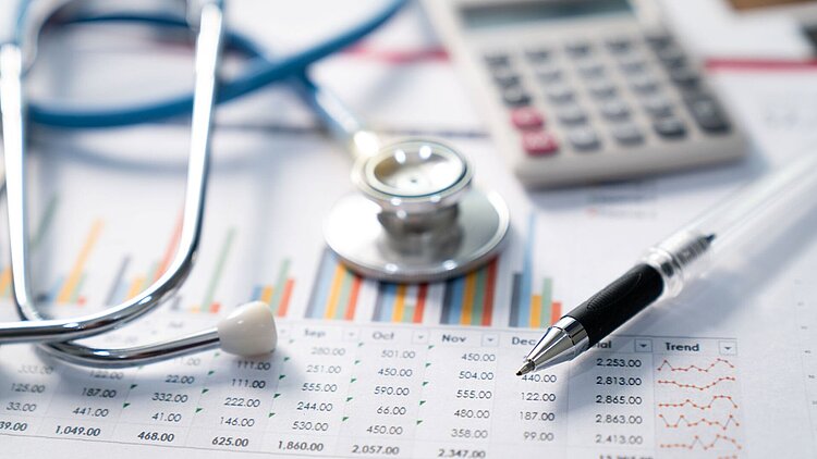 Auf einem Arzt-Schreibtisch liegen Statistiken und ein Taschenrechner für die Planung der Praxisfinanzierung
