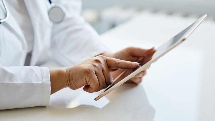 Ein Arzt fährt mit seinem Finger über das Display eines Tablets