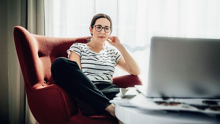 Eine Ärztin sitzt auf einem roten Sessel und liest auf ihrem Laptop das Whitepaper zur Privatabrechnung nach GOÄ.